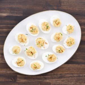 A white serving tray with egg whites stuffed with yolk filling, garnished with paprika and chives.