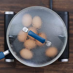 A pan with eggs cooking, covered with a lid, simmering on the stove.