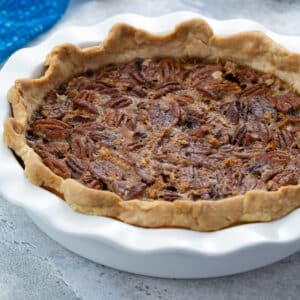 Homemade pecan pie in a white pie dish on a white table, with a blue towel beside it.