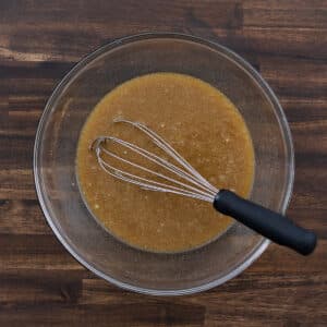 A bowl of prepared pecan pie filling with a whisk placed next to it.