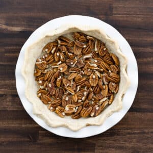 A prebaked pie crust layered with halved pecans, evenly spread.