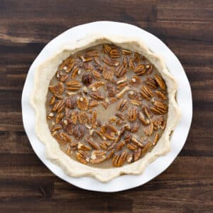 A prebaked pie crust filled with pecans and poured filling, ready for baking.
