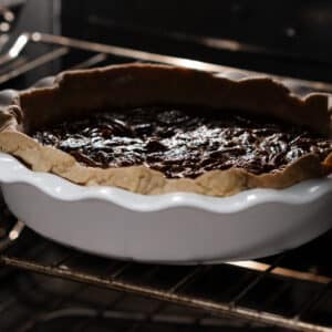 A prebaked pie crust with pecan pie filling baking inside the oven.