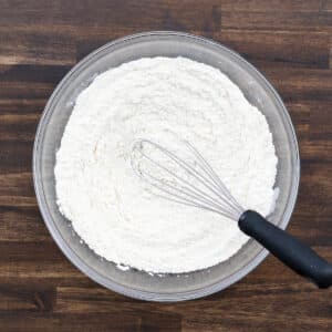 A bowl with flour whisked with salt using a whisk.