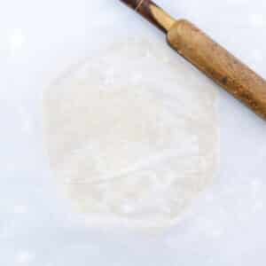 Pie dough on parchment paper, topped with another sheet, being rolled with a rolling pin.