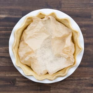 A pie crust in the pie dish lined with parchment paper and topped with rice as pie weight.