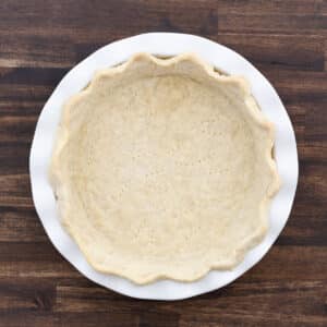 A prebaked pie crust on a wooden table, ready for filling.
