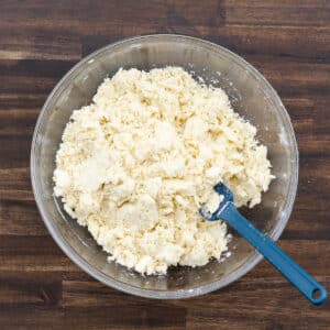 A dough mixture in a bowl being stirred with a blue spatula.
