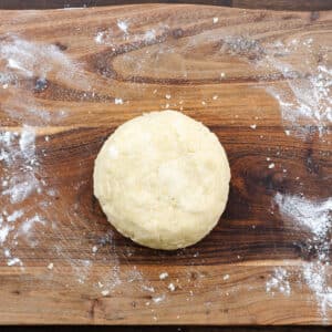 A wooden board with pie crust dough formed into a single disc.