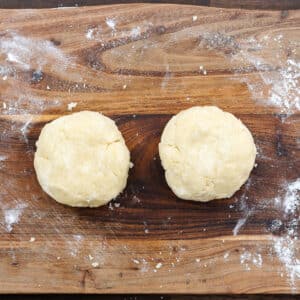 A wooden board with two round discs of pie dough.