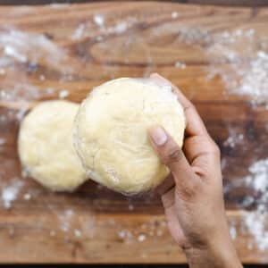 A close-up of a pie dish wrapped in plastic wrap, held in a hand.