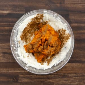 A bowl containing the cream cheese mixture combined with pumpkin puree, pumpkin spice, and vanilla extract.