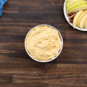 Pumpkin dip served in a white bowl, surrounded by fresh apple slices and crackers for dipping.