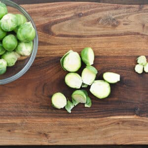 Brussels sprouts sliced in half and ready for cooking, displayed on a wooden cutting board.