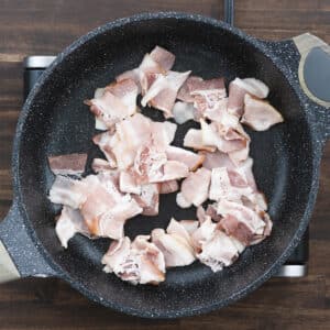 Chopped bacon spread in a pan, beginning to sizzle on medium heat.