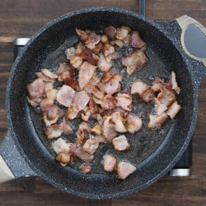 Bacon pieces starting to turn golden brown in the pan, releasing their smoky aroma.