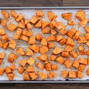 A baking tray lined with parchment paper and arranged sweet potatoes ready to roast.