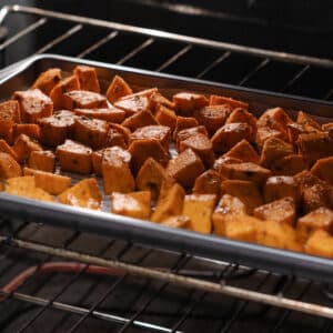 Sweet potatoes roasting inside the oven, caramelizing to golden perfection.