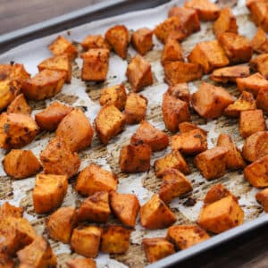 Roasted sweet potatoes served on a parchment-lined baking tray, golden and crispy.