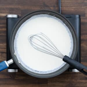 A pan with milk whisked into the roux, forming a lump-free creamy mixture.