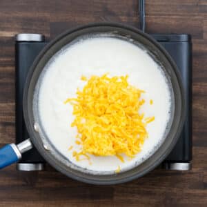 A pan with the milk mixture and shredded cheddar cheese.