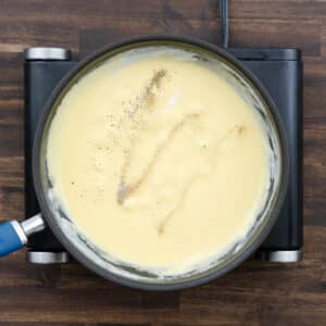 A pan with creamy cheddar cheese sauce, seasoned with black pepper and salt.