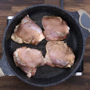 A pan with chicken thighs frying in hot oil, beginning to sear.
