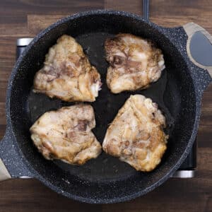 A pan with browned chicken thighs, showcasing a golden, crispy exterior.