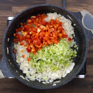 A pan with diced celery and red bell pepper added to the sautéed aromatics.