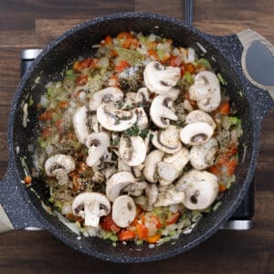 A pan with mushrooms alongside sautéed aromatics and spices.