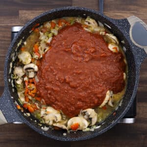 A pan filled with sautéed aromatics, vegetables, and crushed tomatoes.