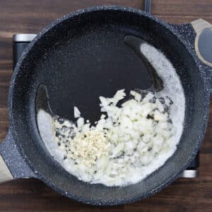A pan with onion and garlic sautéing in melted butter.