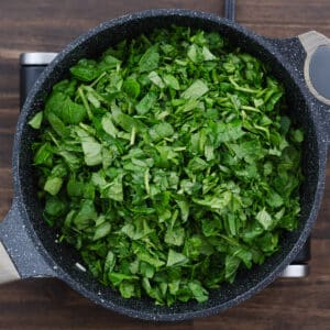 A pan with fresh chopped spinach added to the onion and garlic mixture.