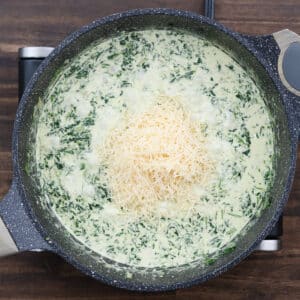 A pan of creamy spinach mixed with melted Parmesan cheese.