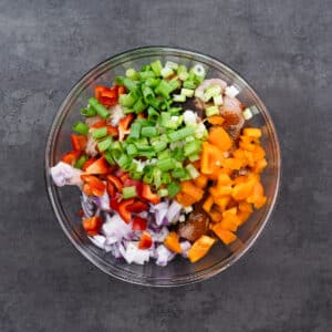 A bowl filled with chicken, fresh veggies, aromatics, and spices ready for marination.