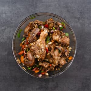 A bowl of chicken marinated with spices, aromatics, and vegetables for Jamaican Brown Stew Chicken.