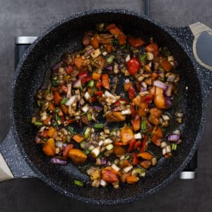 A pan with sautéed aromatics and colorful veggies, releasing fragrant flavors.