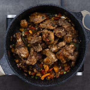 A pan combining seared chicken with sautéed veggies and aromatics, ready for the next step.