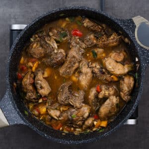 A pan filled with seared chicken, vegetables, aromatics, and flavorful chicken broth.