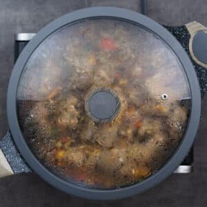 A pan with chicken and aromatics simmering gently under a closed lid.