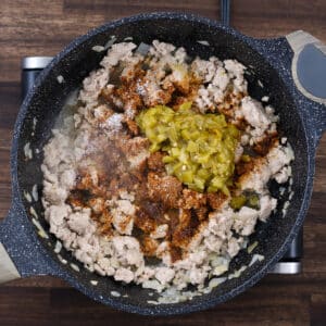 A pan with seasoned ground meat, taco seasoning, salt, and green chiles mixed together.