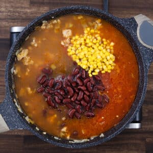 A pan with seasoned ground meat, beans, corn, crushed tomatoes, and savory broth combined.