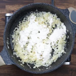 A pan with sautéed onions and garlic, sprinkled with all-purpose flour.