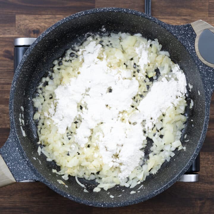 A pan with sautéed onions and garlic, sprinkled with all-purpose flour.
