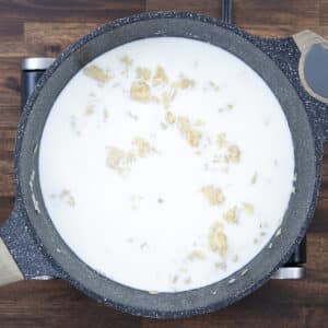 A pan with sautéed onions and garlic mixed with a roux and milk.