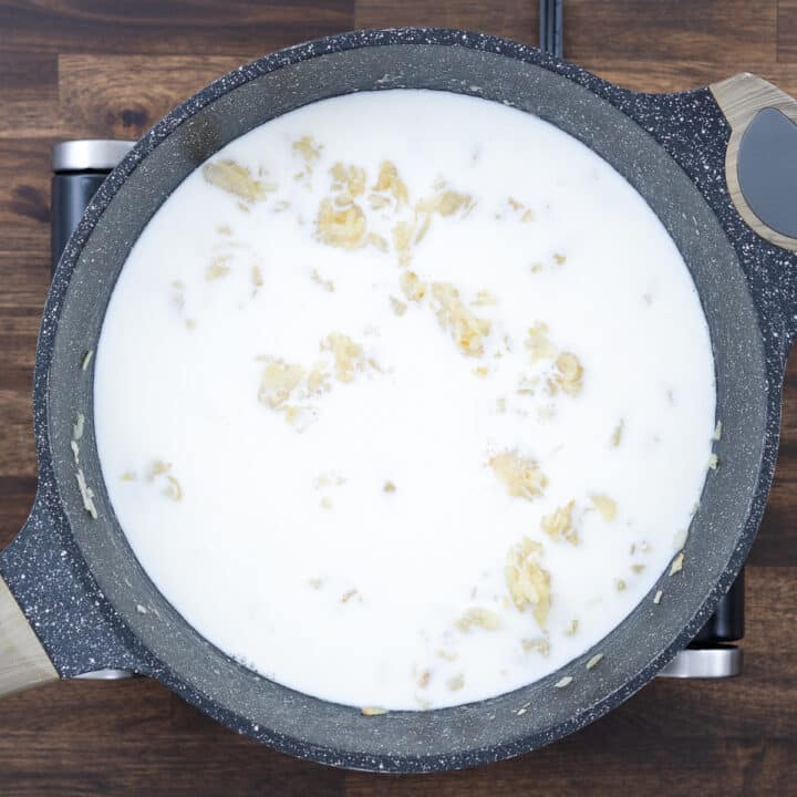 A pan with sautéed onions and garlic mixed with a roux and milk.