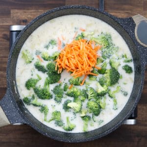A pan with broccoli and carrots simmering in a milk and broth mixture.