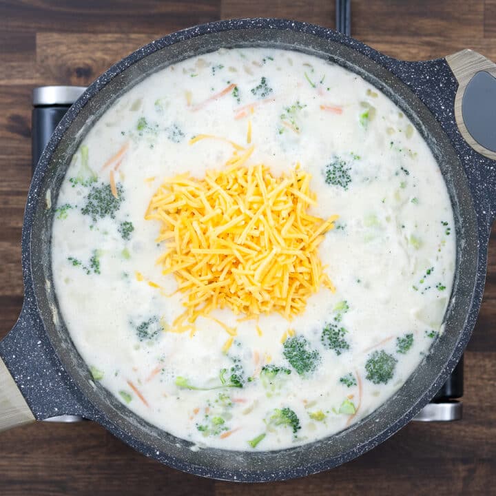 A pan with broccoli and carrots in a milk mixture, with freshly added shredded cheddar cheese.
