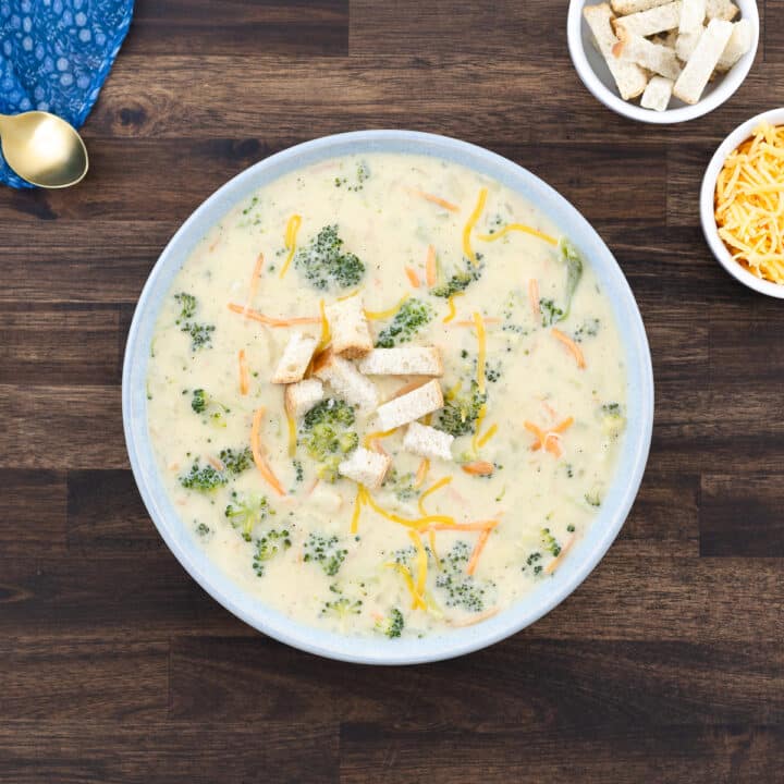A bowl of broccoli cheddar soup, garnished with croutons and shredded cheddar cheese.