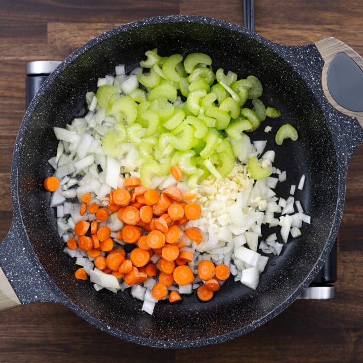 A pan with aromatics and vegetables ready for sautéing.